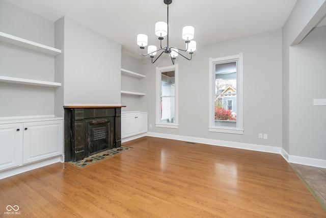 unfurnished living room with built in features, a fireplace, a notable chandelier, and light wood-type flooring