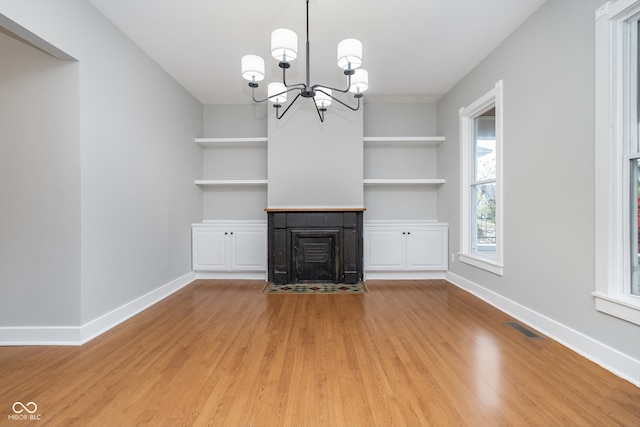 unfurnished living room with built in shelves, light wood-type flooring, and an inviting chandelier