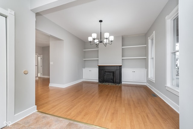 unfurnished living room with built in shelves, light wood-type flooring, and a chandelier