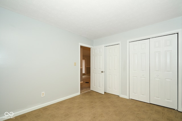 unfurnished bedroom with a textured ceiling, light carpet, and multiple closets