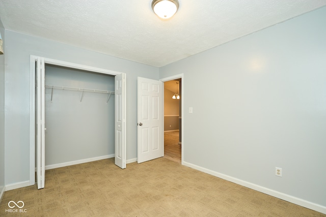 unfurnished bedroom with light colored carpet, a textured ceiling, and a closet