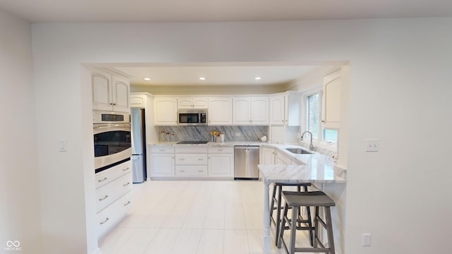 kitchen with white cabinetry, sink, light stone countertops, stainless steel appliances, and a kitchen bar