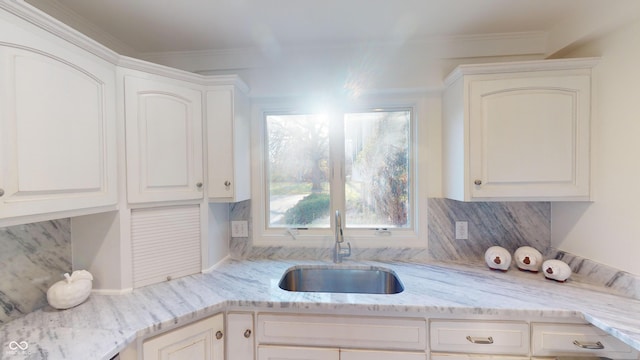 kitchen with decorative backsplash, light stone countertops, crown molding, sink, and white cabinets