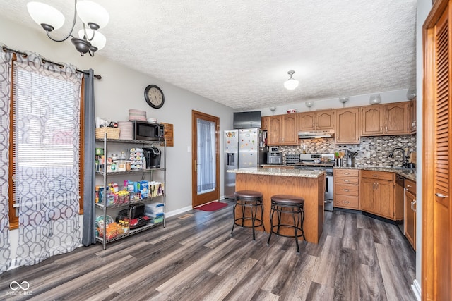 kitchen featuring a textured ceiling, stainless steel appliances, a notable chandelier, dark hardwood / wood-style floors, and a kitchen island