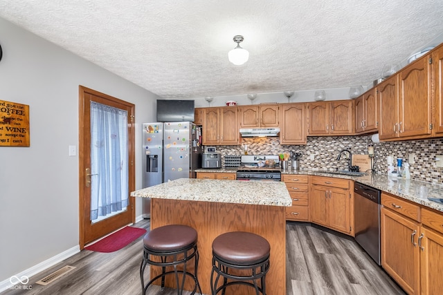 kitchen with sink, dark hardwood / wood-style floors, appliances with stainless steel finishes, a kitchen island, and a breakfast bar area