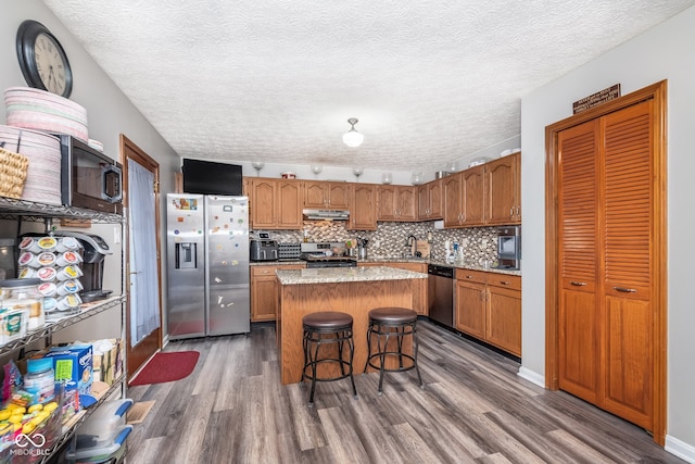 kitchen with appliances with stainless steel finishes, dark hardwood / wood-style flooring, a textured ceiling, a kitchen island, and a breakfast bar area