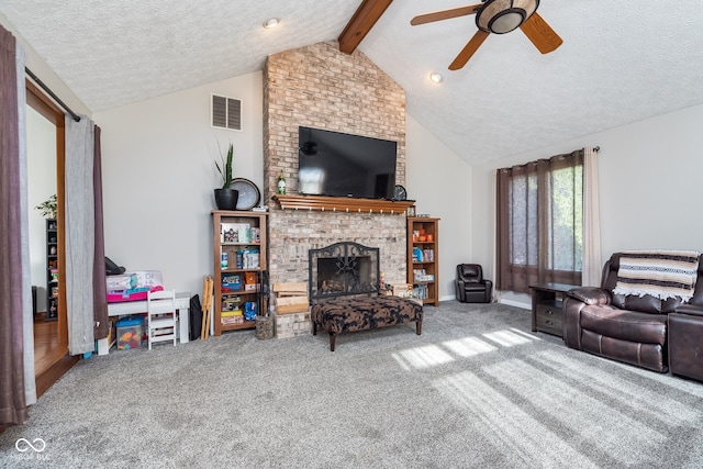 living room with a brick fireplace, a textured ceiling, carpet floors, ceiling fan, and vaulted ceiling with beams