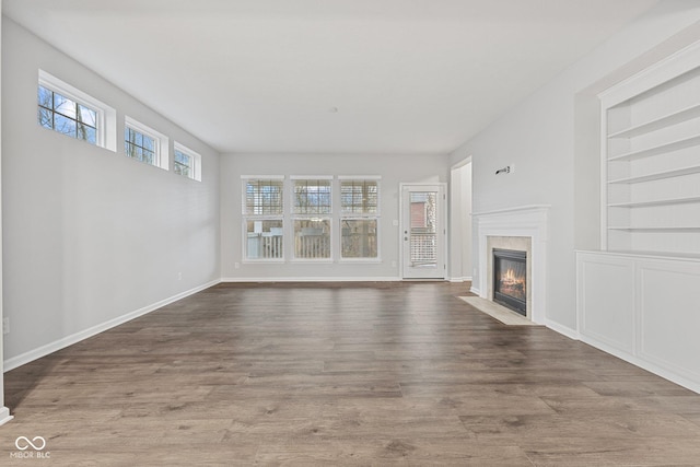 unfurnished living room with built in shelves and hardwood / wood-style floors