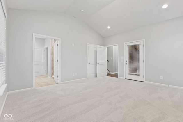 unfurnished bedroom with ensuite bath, light colored carpet, and vaulted ceiling