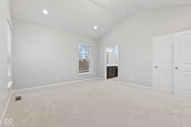 unfurnished bedroom featuring a textured ceiling, connected bathroom, light colored carpet, and lofted ceiling