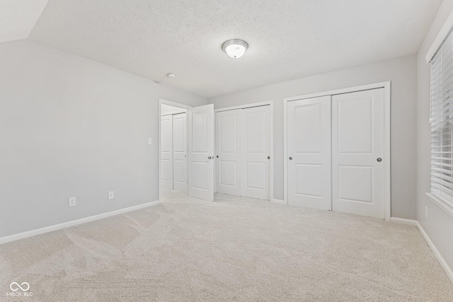 unfurnished bedroom featuring carpet, vaulted ceiling, a textured ceiling, and two closets