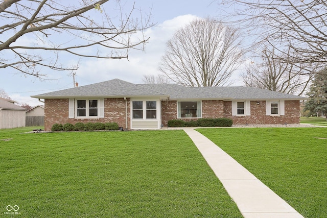 ranch-style home featuring brick siding, a front yard, and roof with shingles