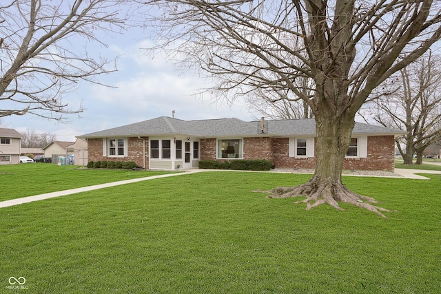 view of front of home featuring brick siding, a front yard, and a shingled roof