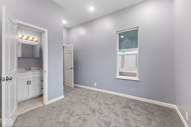 unfurnished bedroom featuring ensuite bath, light carpet, and sink