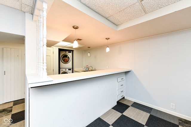 kitchen featuring kitchen peninsula, dark carpet, sink, decorative light fixtures, and stacked washer / dryer