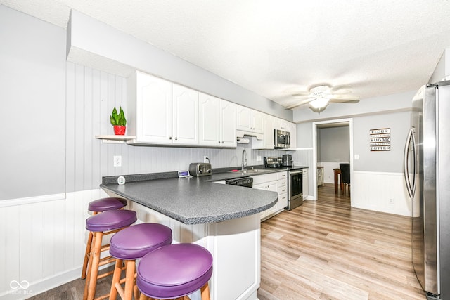 kitchen with white cabinetry, stainless steel appliances, kitchen peninsula, a breakfast bar area, and light wood-type flooring