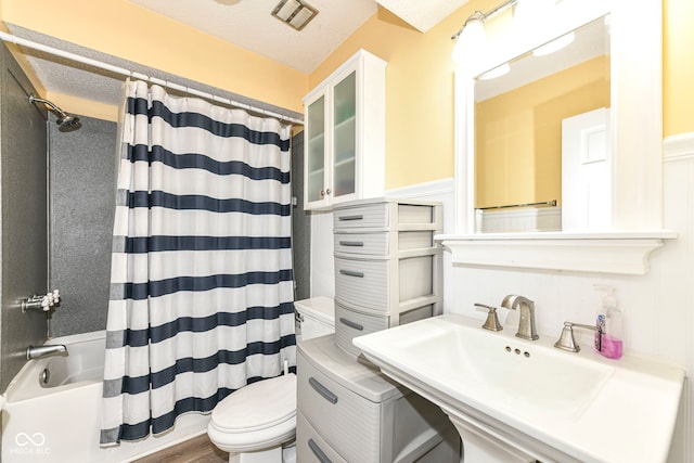 full bathroom with hardwood / wood-style floors, sink, toilet, shower / bathtub combination with curtain, and a textured ceiling