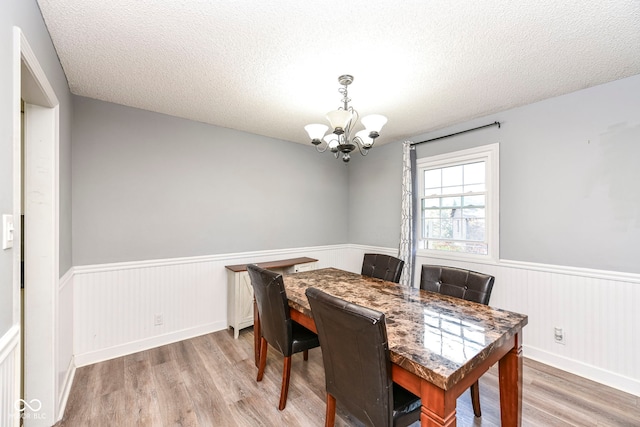 dining room with light hardwood / wood-style floors, a textured ceiling, and an inviting chandelier