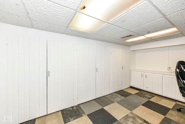 basement with a paneled ceiling and wood walls