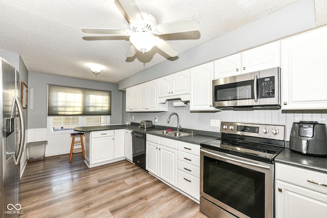 kitchen featuring appliances with stainless steel finishes, a textured ceiling, sink, light hardwood / wood-style flooring, and white cabinets