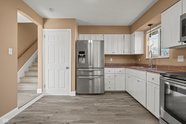 kitchen with sink, stainless steel appliances, white cabinetry, and light hardwood / wood-style flooring