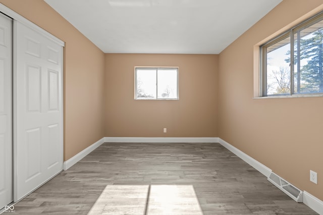 unfurnished bedroom with light wood-type flooring, a closet, and multiple windows