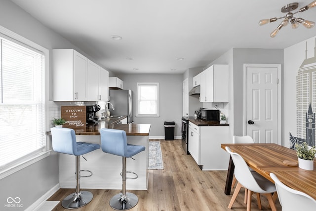 kitchen featuring white cabinets, appliances with stainless steel finishes, light hardwood / wood-style floors, and a breakfast bar area