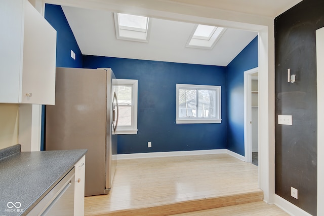 kitchen with light wood-type flooring, white cabinetry, stainless steel refrigerator, and vaulted ceiling with skylight