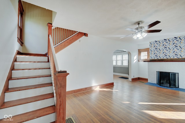 stairs with ceiling fan, wood-type flooring, and a brick fireplace