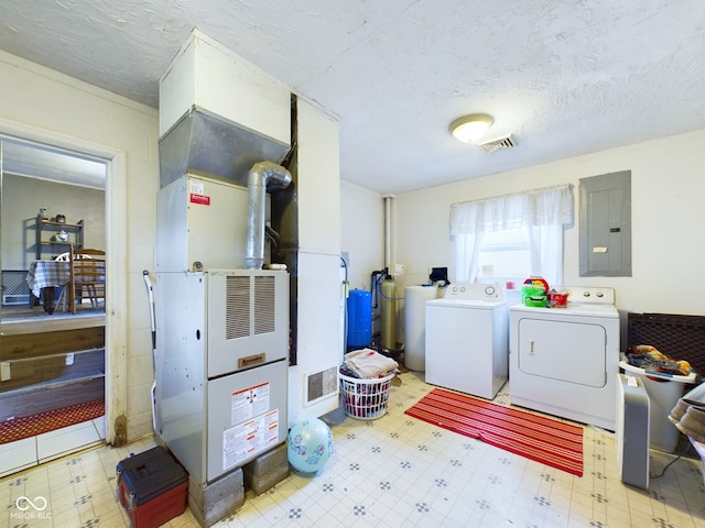 washroom with a textured ceiling, heating unit, electric panel, and washer and clothes dryer