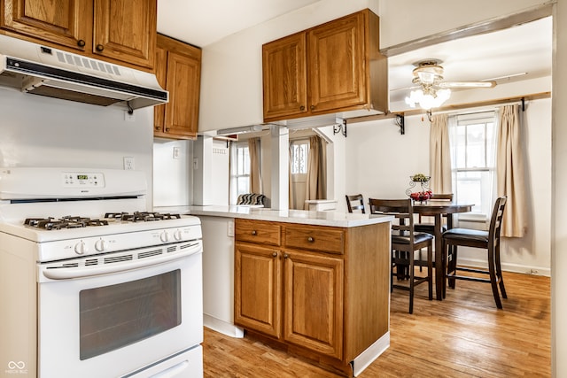 kitchen featuring kitchen peninsula, gas range gas stove, ceiling fan, and light wood-type flooring