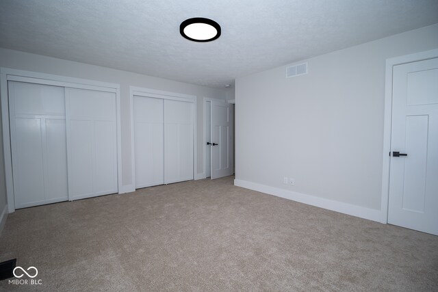 unfurnished bedroom featuring a textured ceiling, light carpet, and two closets