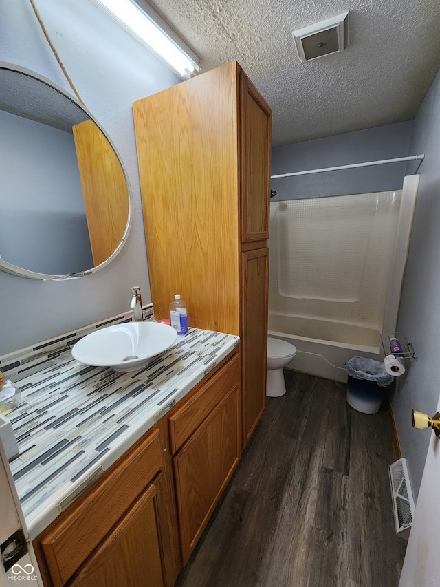 full bathroom featuring toilet, wood-type flooring, a textured ceiling, vanity, and shower / bath combination