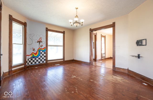 spare room with wood-type flooring, a wealth of natural light, and a chandelier