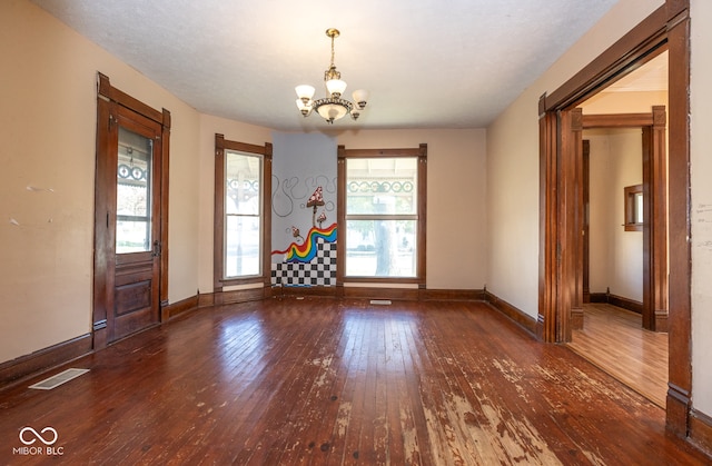 spare room with dark wood-type flooring and an inviting chandelier