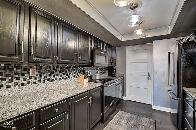 kitchen with light stone countertops, appliances with stainless steel finishes, decorative backsplash, a raised ceiling, and dark tile patterned flooring