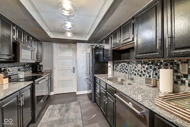 kitchen featuring sink, a raised ceiling, light stone counters, decorative backsplash, and appliances with stainless steel finishes