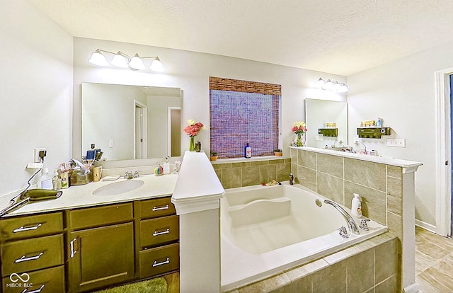 bathroom with vanity, a relaxing tiled tub, and a textured ceiling