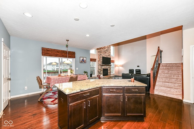 kitchen with dark brown cabinets, a kitchen island, a stone fireplace, and dark wood-type flooring