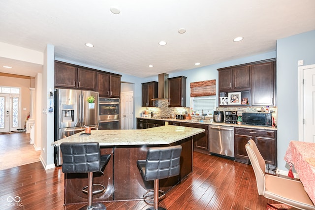 kitchen featuring a center island, wall chimney range hood, stainless steel appliances, and a breakfast bar area