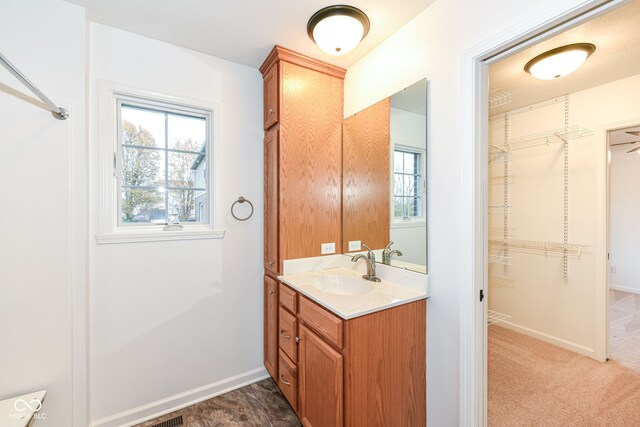 bathroom with a walk in closet, vanity, and baseboards