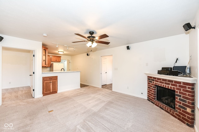 unfurnished living room featuring a fireplace, light colored carpet, a ceiling fan, track lighting, and baseboards