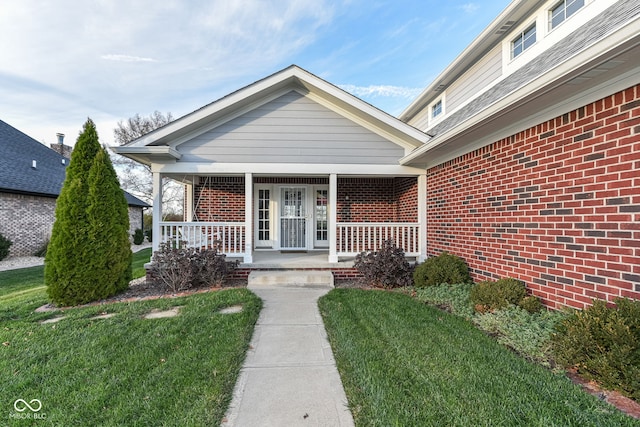 entrance to property featuring covered porch, a yard, and brick siding