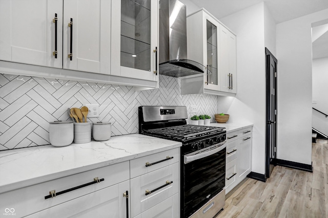 kitchen with light stone countertops, stainless steel gas range, wall chimney range hood, light hardwood / wood-style floors, and white cabinetry