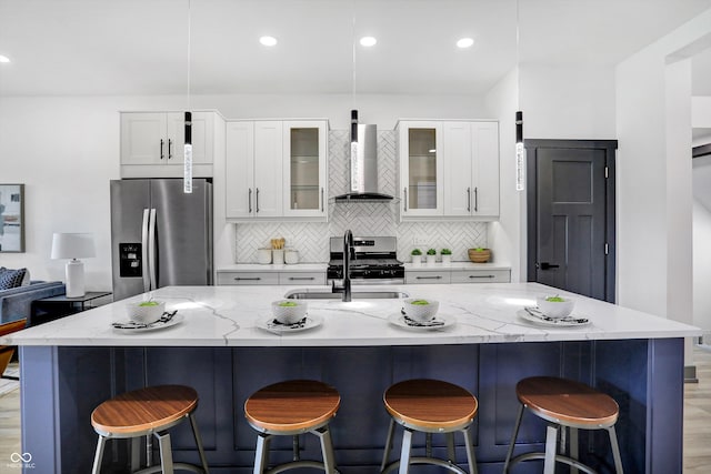 kitchen with appliances with stainless steel finishes, light hardwood / wood-style flooring, a kitchen island with sink, and wall chimney exhaust hood