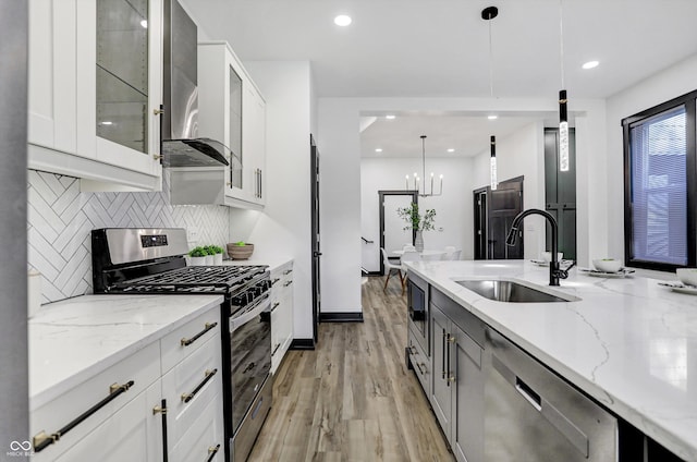 kitchen featuring sink, stainless steel appliances, wall chimney range hood, light stone counters, and decorative light fixtures