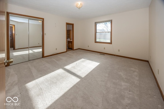 unfurnished bedroom with ensuite bathroom, a closet, and light colored carpet