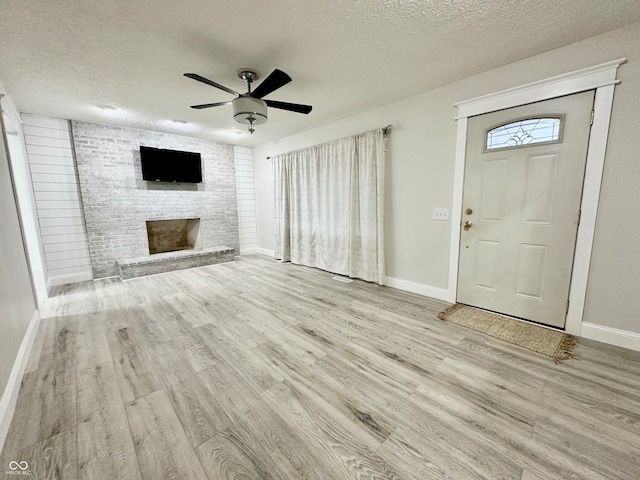 entryway featuring a fireplace, a textured ceiling, light wood-type flooring, and ceiling fan