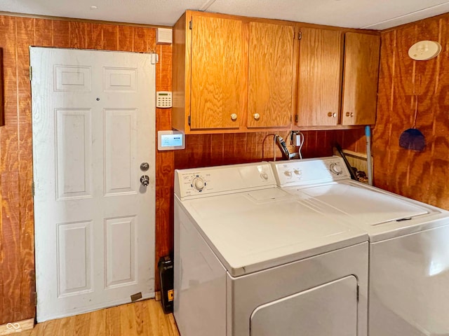 clothes washing area featuring cabinets, a textured ceiling, washer and clothes dryer, wooden walls, and light hardwood / wood-style floors