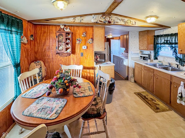 dining area with lofted ceiling with beams, wood walls, washing machine and dryer, and sink